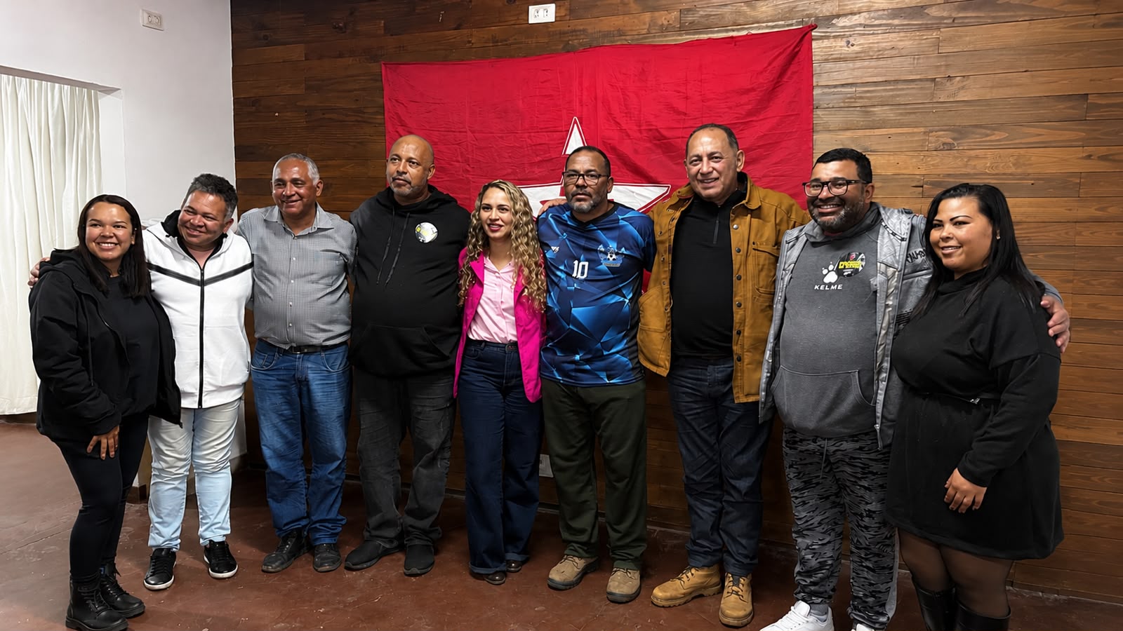 Grupo de pessoas posa para foto em frente a uma bandeira do Partido dos Trabalhadores (PT).