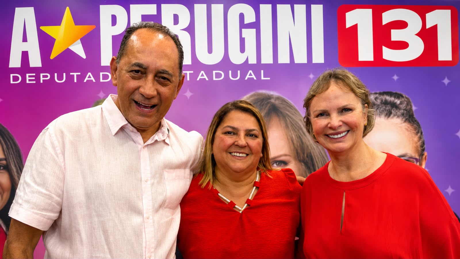 João Paulo aparece ao lado de Ana Perugini e de uma liderança política, sorrindo para a câmera durante um encontro em Hortolândia. Ao fundo, há um painel de campanha de Ana Perugini para deputada estadual, com o número 131.