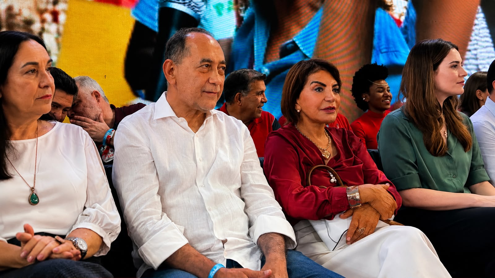 João Paulo aparece sentado entre outras lideranças durante um evento, acompanhado por pessoas de diferentes gerações. Ao fundo, um grande painel exibe imagens relacionadas à atividade.