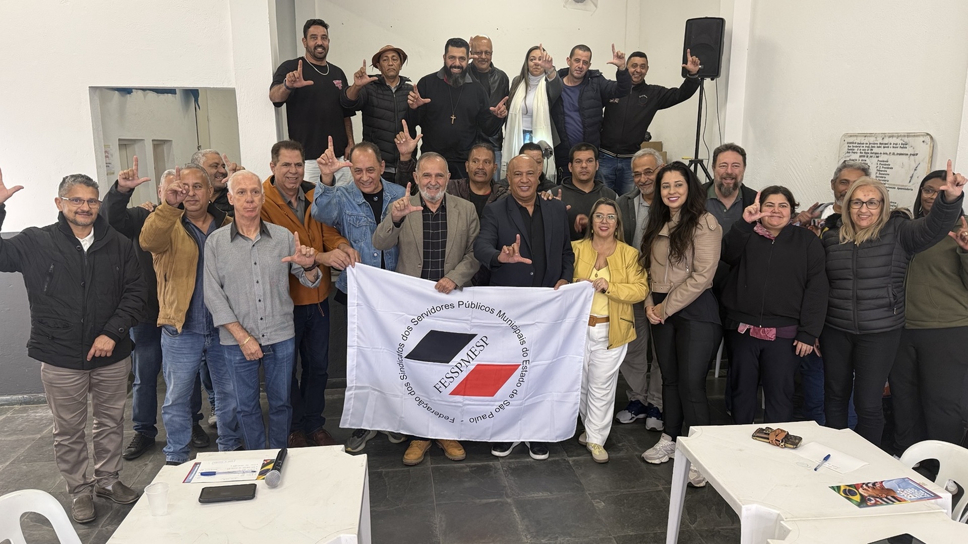 Grupo de pessoas reunidas em frente à bandeira da FESSPMESP durante encontro com representantes dos servidores públicos municipais.
